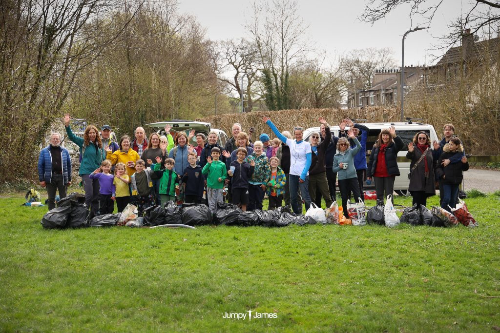 A large group of volunteers stands behind a collection of bin bags that they've used to collect rubbish. 