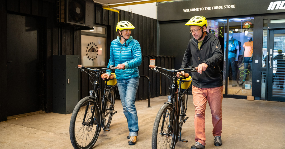 Two people walking with e-bikes, wearing helmets.