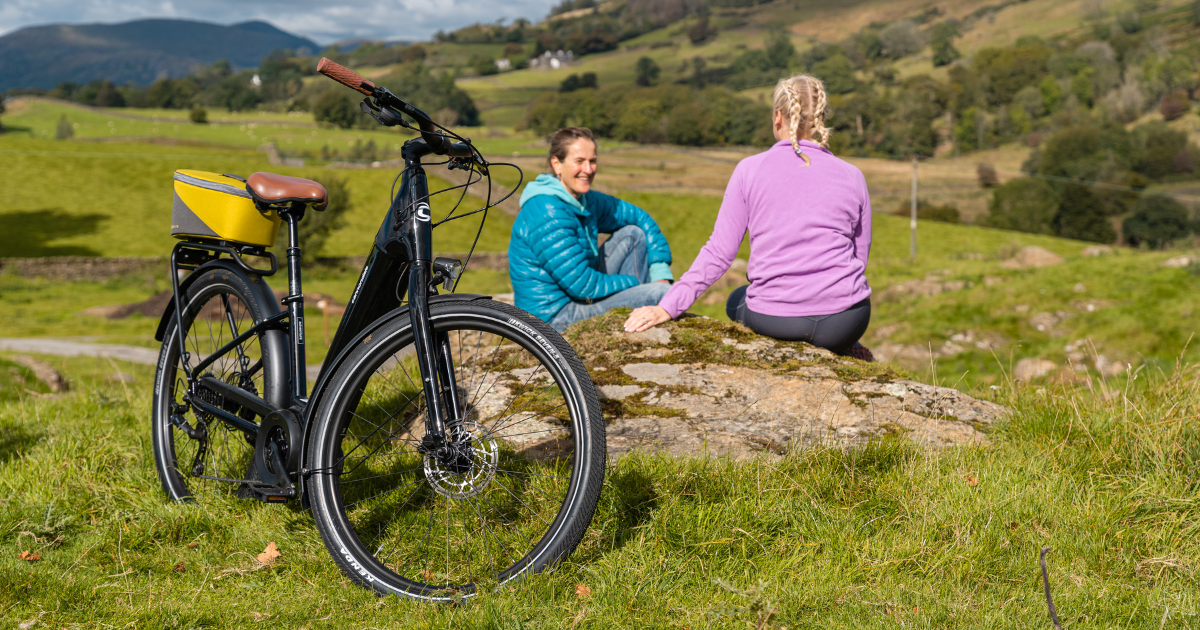 Two people sitting chatting on the fells with ebikes in the foreground