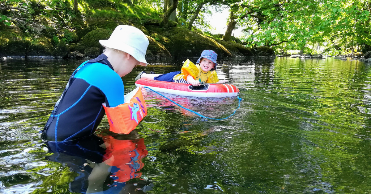 Two young children playing in the waters of the river Kent with arm bands and an inflatable dinghy.