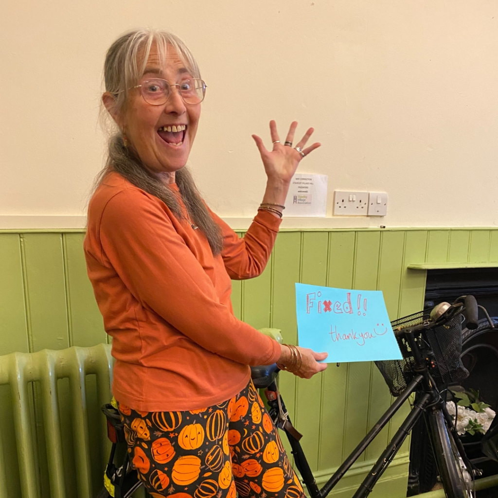 A smiling person at the Sustainable Staveley repair café standing in front of their newly fixed bike with a sign that says 'fixed!'