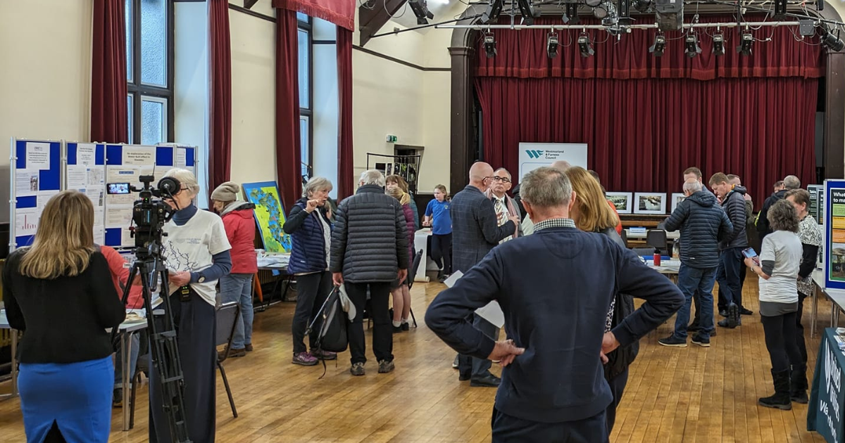 A photograph of people in the hall at The Institute, Staveley,  which is decked out with stalls about the river Kent & water quality, as part of the United Utilities drop-in event. 