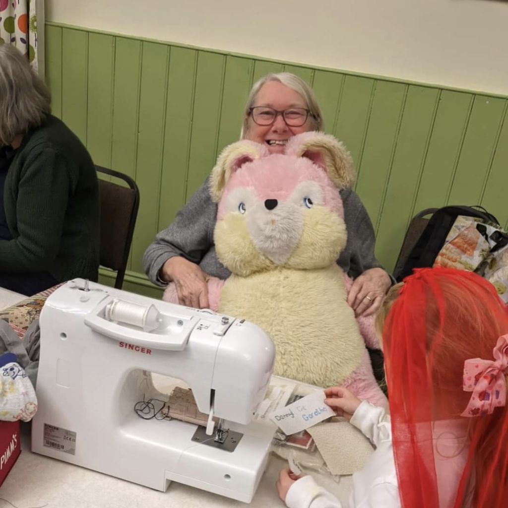 A volunteer repairer at the Staveley Repair Café, with a giant teddy they've just fixed on their lap and a sewing machine in front of them. 