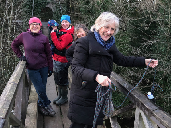A group of people of various ages smiling while standing on a bridge over the river Kent