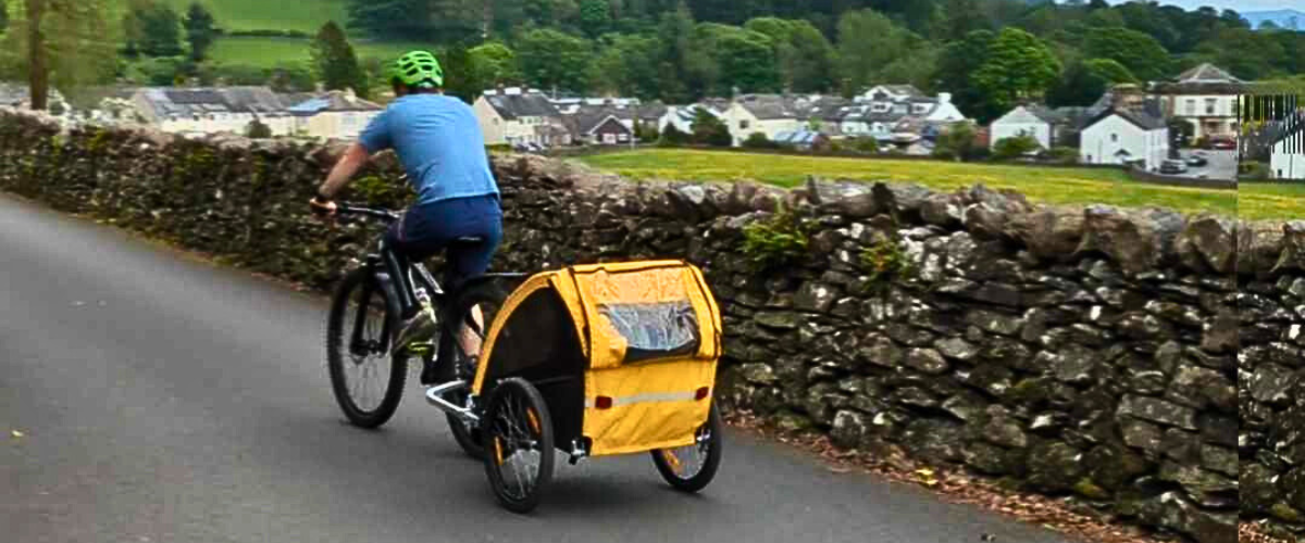 A person cycling along a Staveley lane on an ebike, towing a trailer behind them.